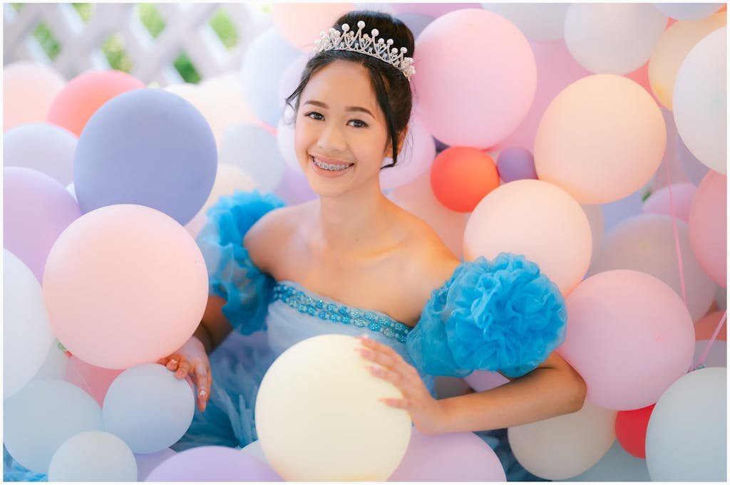A young woman dressed in blue surrounded by colorful balloons, smiling joyfully.