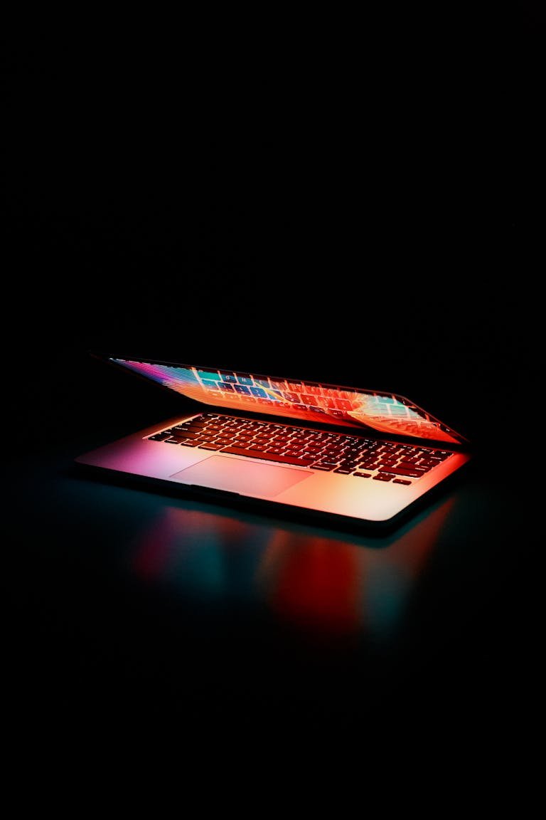 Mac Računala Laptop partially opened, emitting vibrant multicolored lights in dark setting.