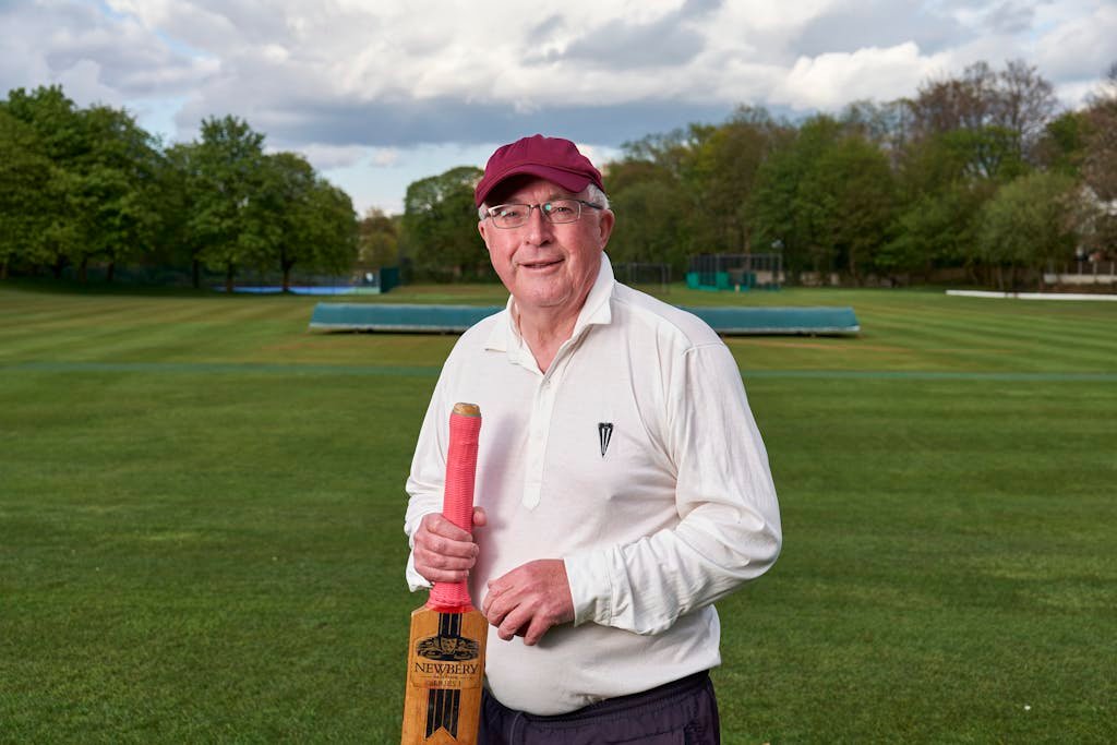 Wheon Cricket 07 Senior man with cricket bat standing on a lush outdoor field ready for a game.