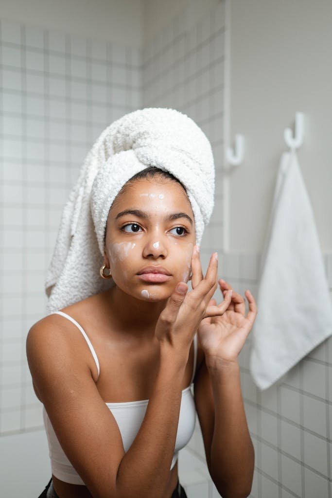 Young woman Skin Care in Hindi Wellhealthorganic with a towel on her head applying skincare cream in a modern bathroom.
